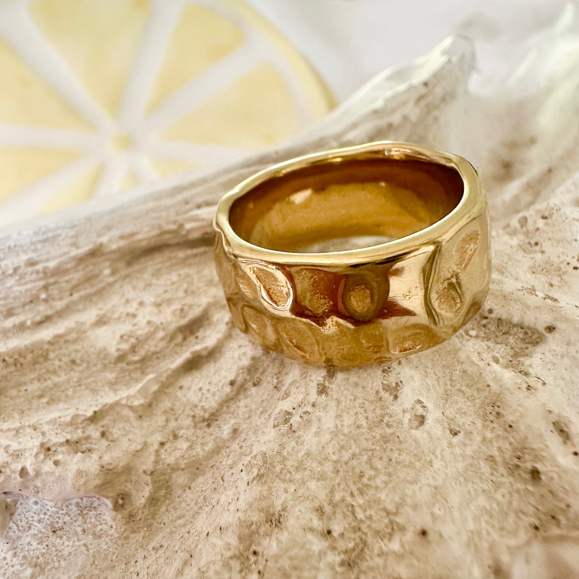 EVER Signal Ring displayed on a white shell with a lemon slice in the background, showcasing its bold hammered gold texture.