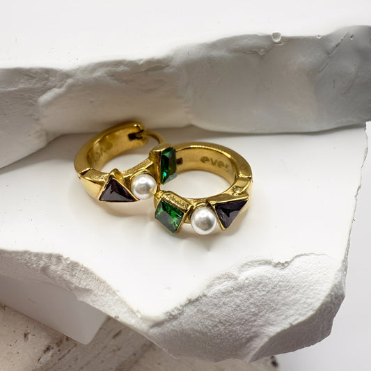 Gold hoop earrings with gemstones and pearls on a white stone surface