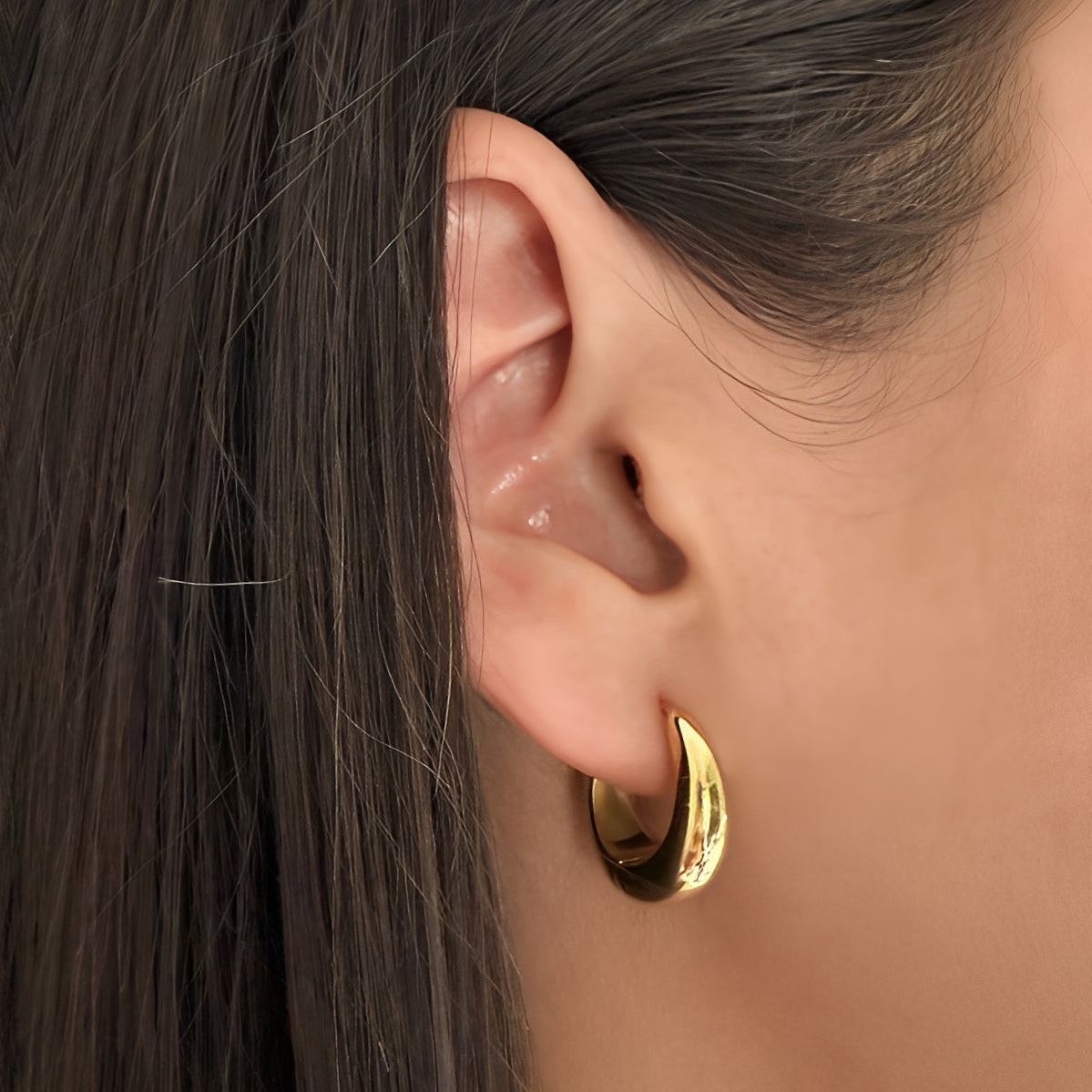Gold hoop earring worn by a person with dark hair.