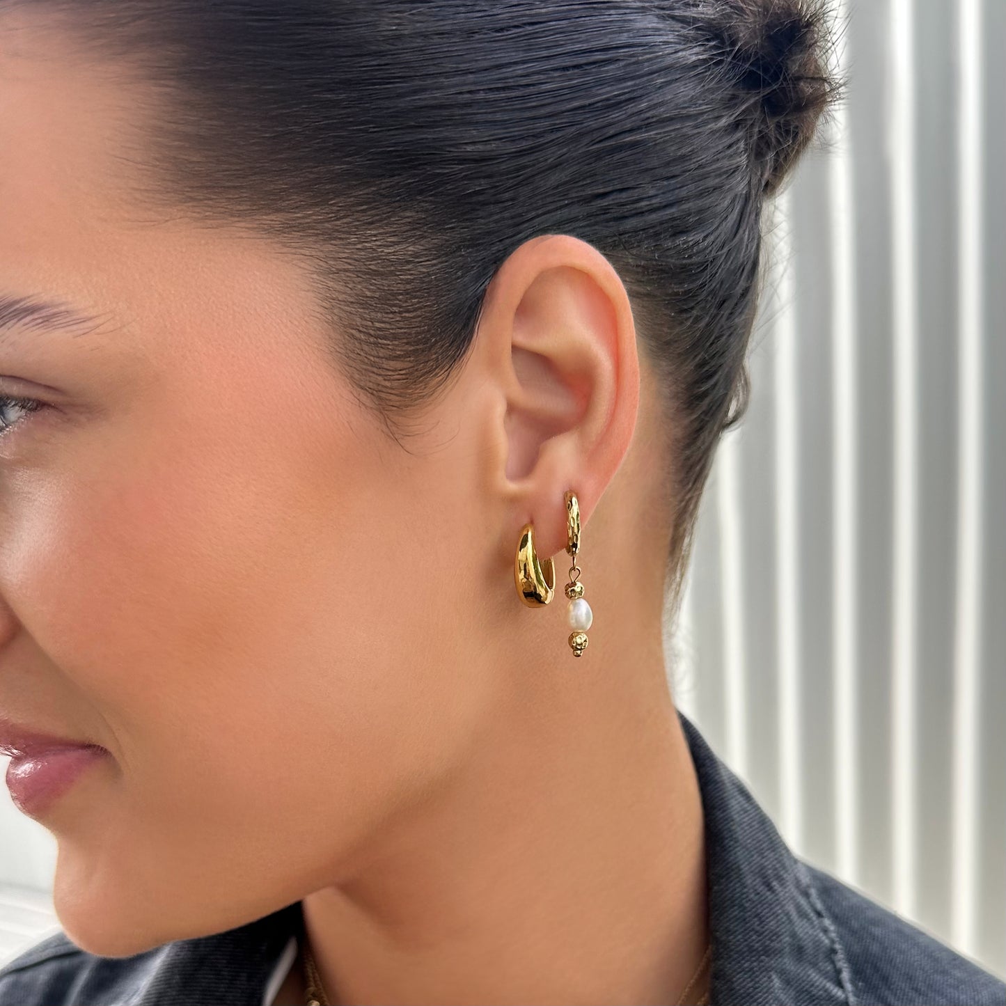 Close-up of a woman wearing gold hoop earrings with pearl accents.