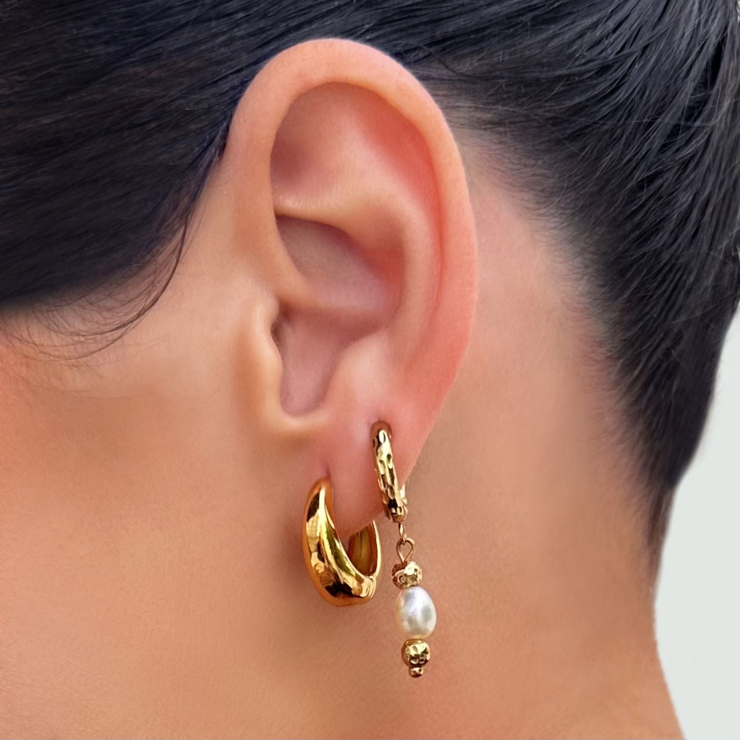 Gold hoop earring with pearl drop worn by a person