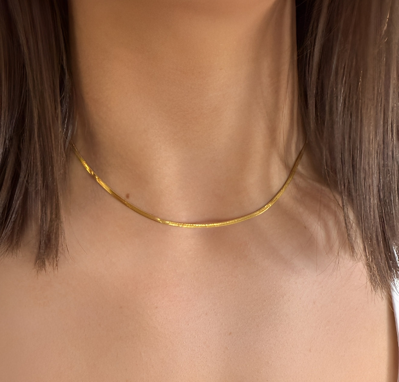 Gold necklace on a person with a neutral background