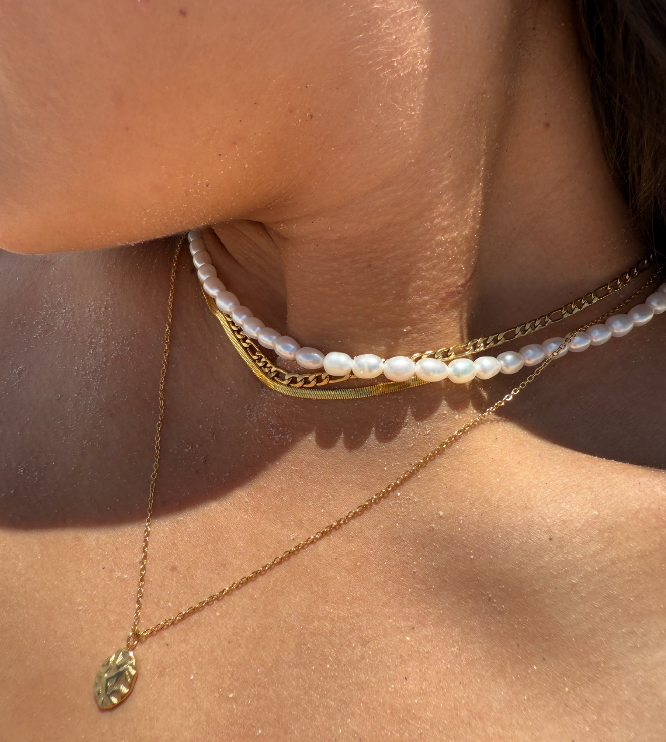 Close-up of a person wearing gold and pearl necklaces on a sunlit background