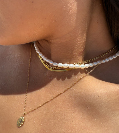 Close-up of a person wearing gold and pearl necklaces on a sunlit background