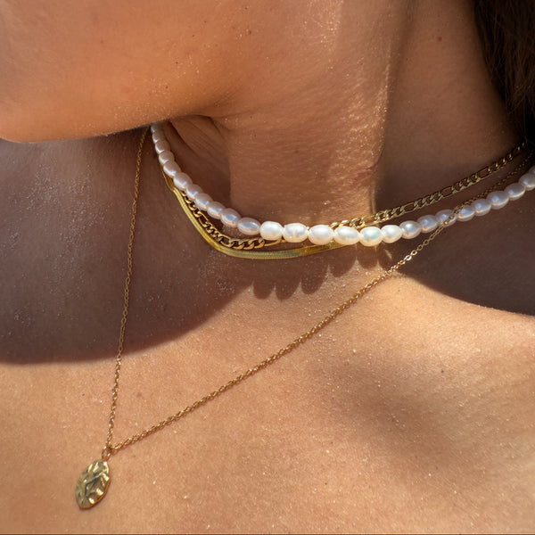 Close-up of a person wearing gold and pearl necklaces on a sunlit background