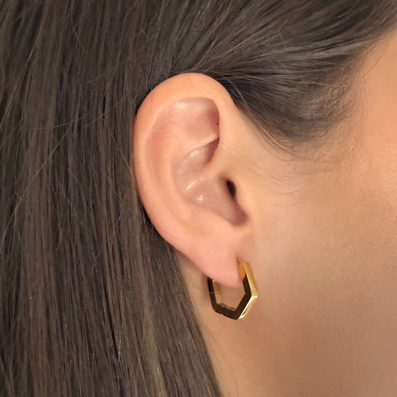 Close-up of an ear wearing a gold hexagonal earring with hair partially covering the frame.