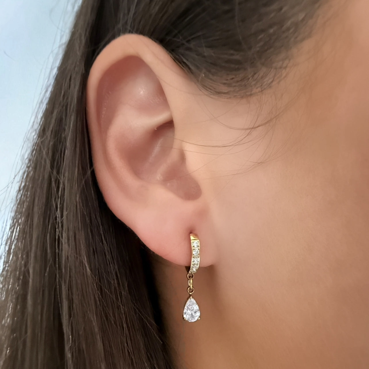 Close-up of a person wearing a gold earring with a teardrop design.