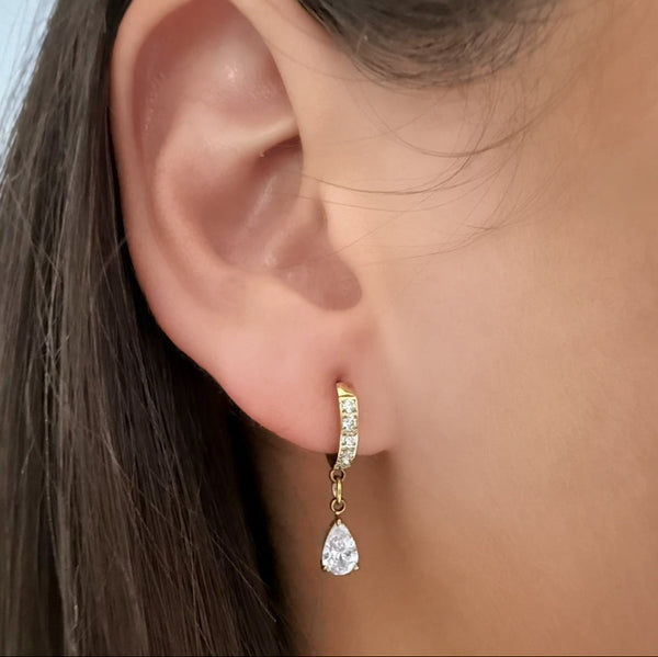 Close-up of a person wearing a gold earring with a teardrop design.