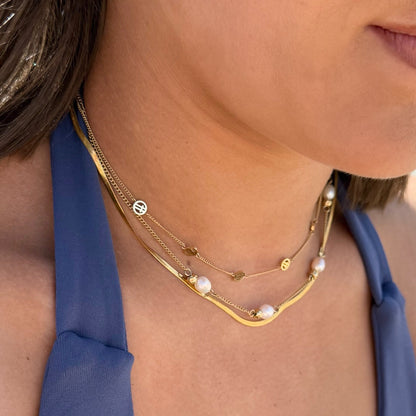 Close-up of a person wearing a gold necklace with pearl accents against a blue garment.