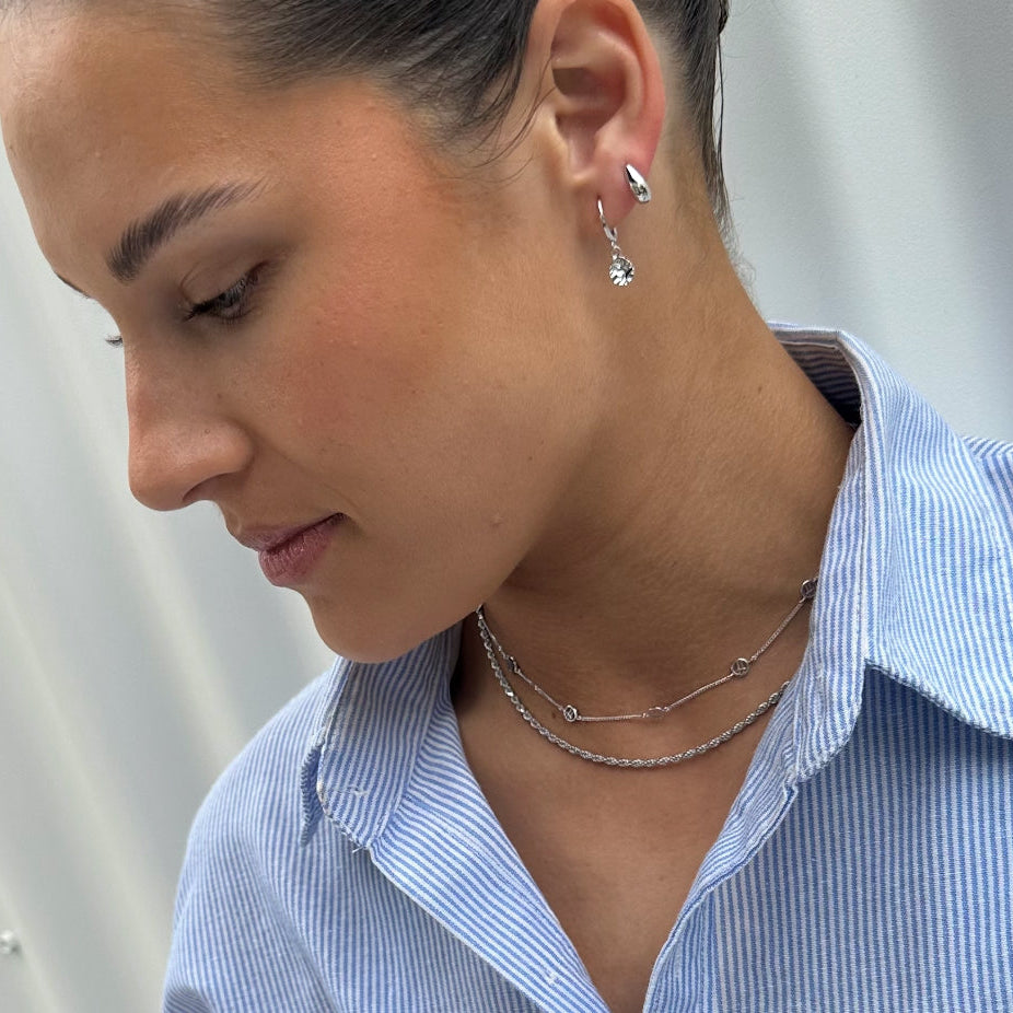Close-up of a person wearing silver earrings and necklaces against a neutral background