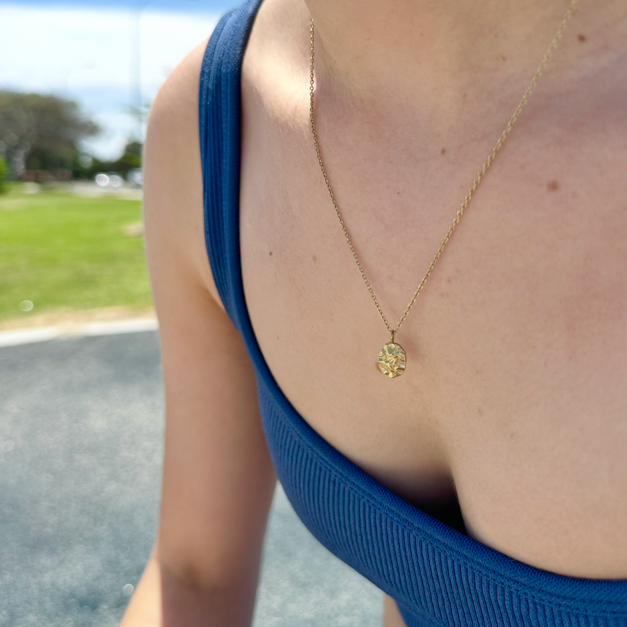Person wearing a gold necklace with a blue top outdoors