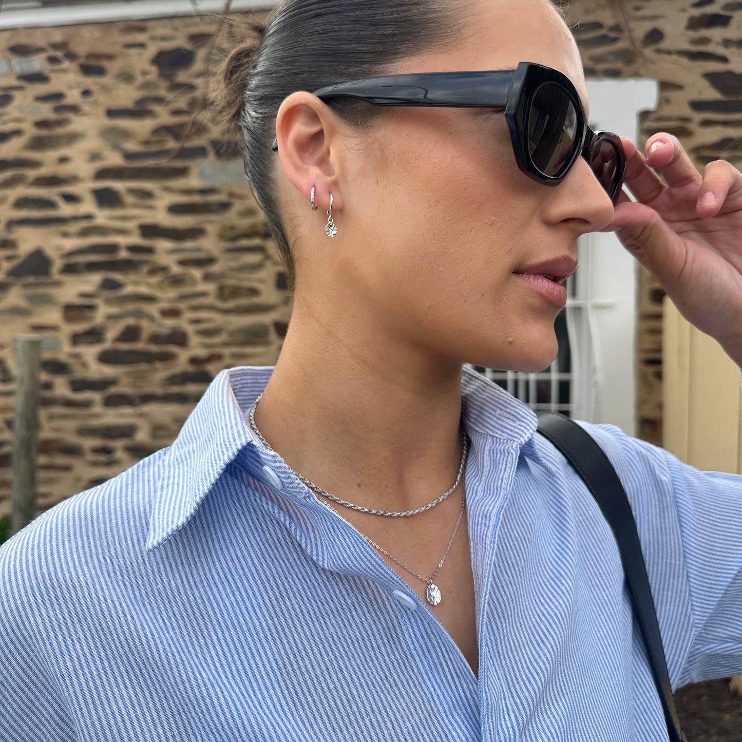 Woman adjusting sunglasses wearing Silver Harmony Earringswith a stone wall background