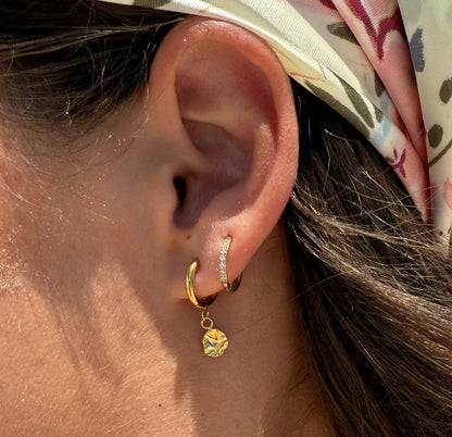 Close-up of an ear wearing gold hoop earrings with a floral headband.