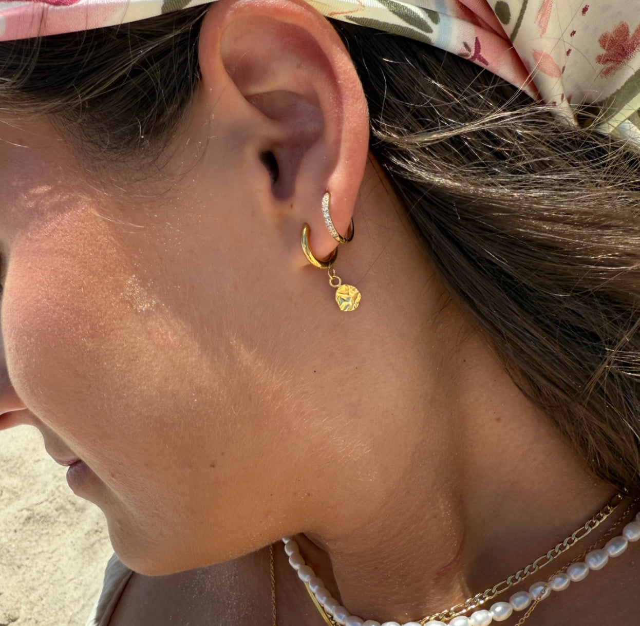 Close-up of a person wearing gold hoop earrings and a pearl necklace with a blurred background.