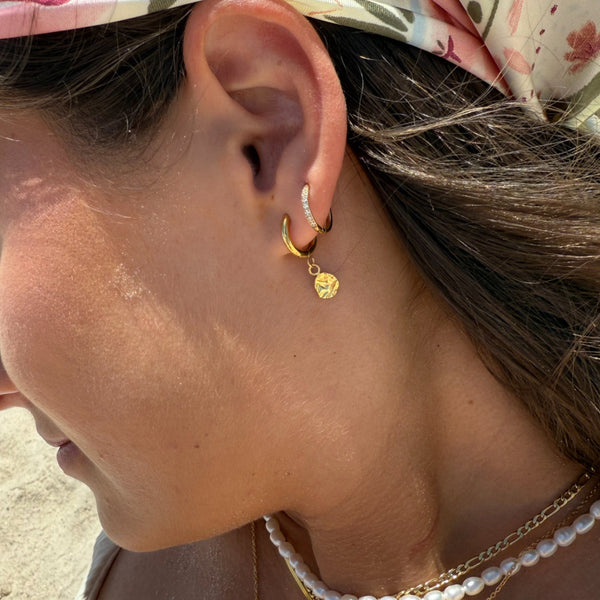 Close-up of a person wearing gold hoop earrings and a pearl necklace with a blurred background.