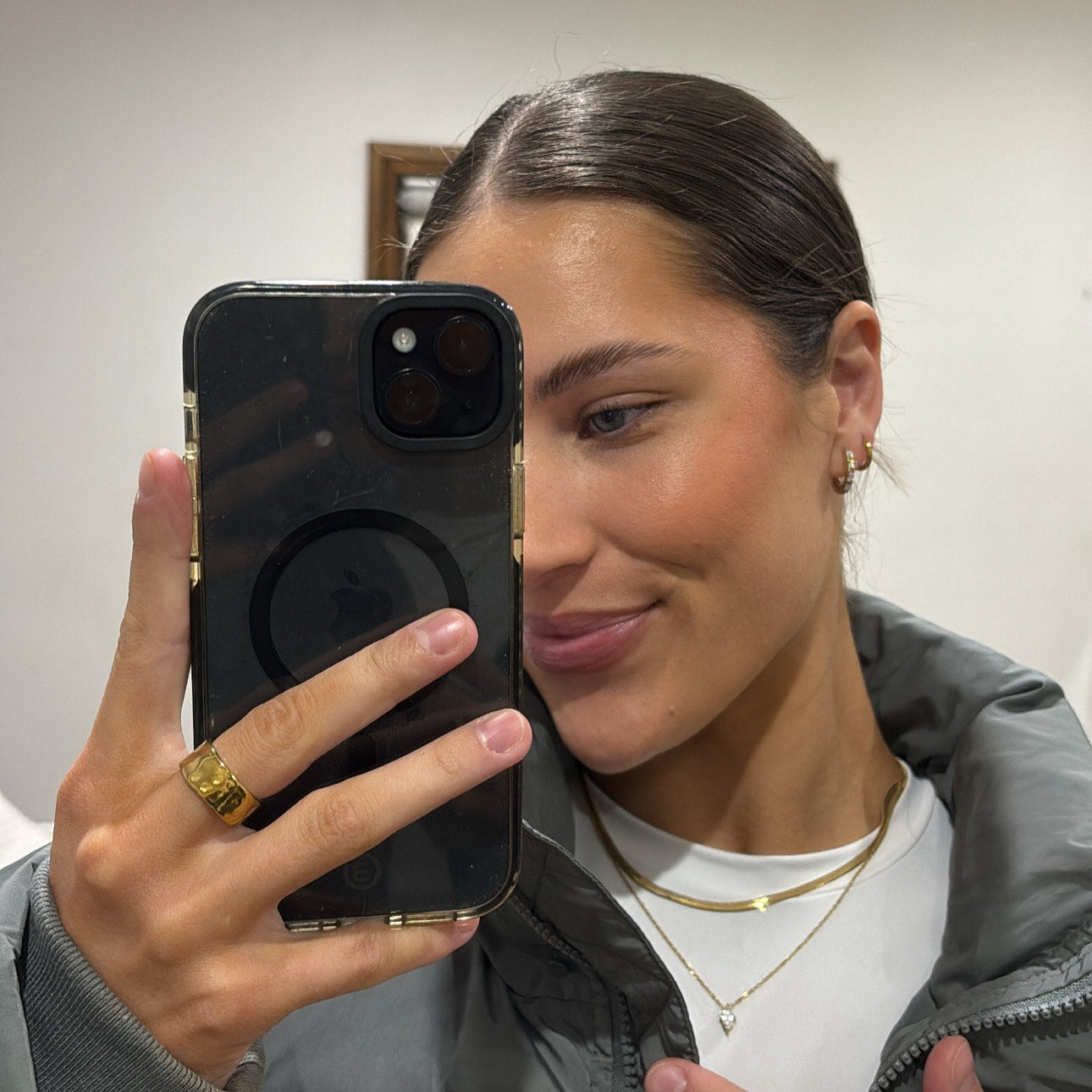 Person taking a mirror selfie wearing a gray jacket and white shirt.