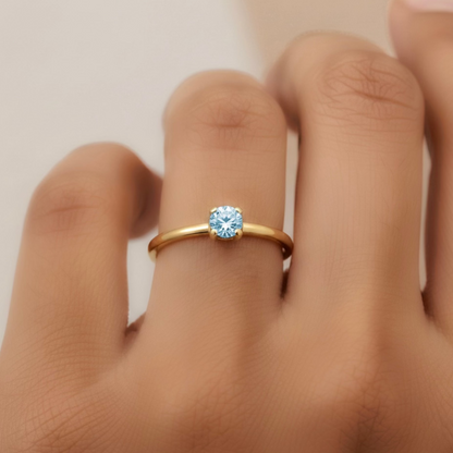 Gold ring with a aquamarine on a person's finger against a neutral background