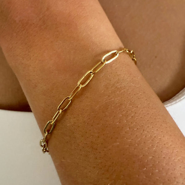Gold chain bracelet on a wrist against a neutral background