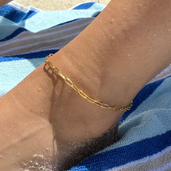 Gold anklet on a person's ankle with a striped towel in the background