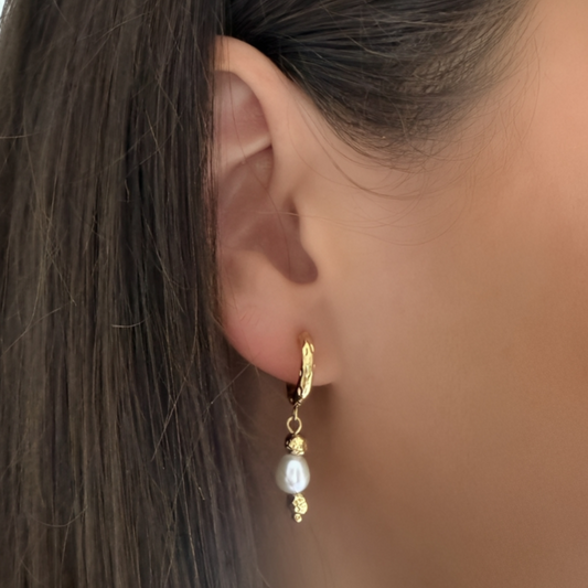 Close-up of an ear wearing a gold earring with a pearl drop.