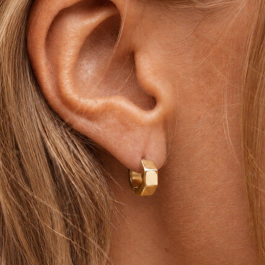 A close-up of a model's ear wearing a small gold huggie hoop earring.
