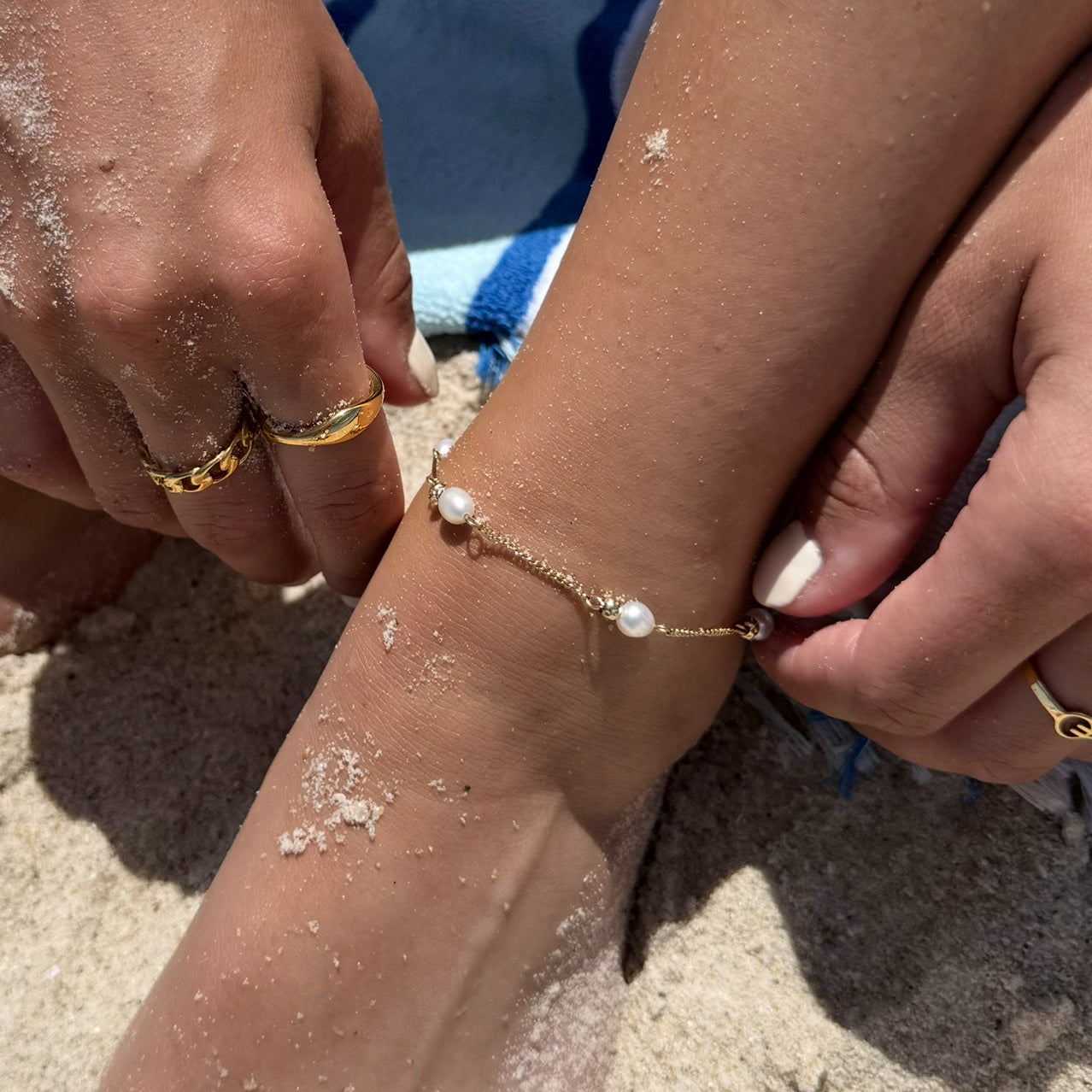Close-up of a hand wearing a gold bracelet with pearls on a sandy background