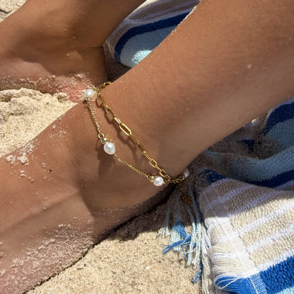 Gold bracelet with pearls on a person's wrist by the sand