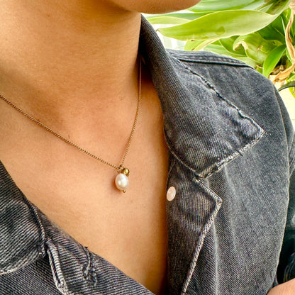 Person wearing the Off Court Pearl Necklace, gold necklace with a pearl pendant, standing outdoors with greenery in the background.