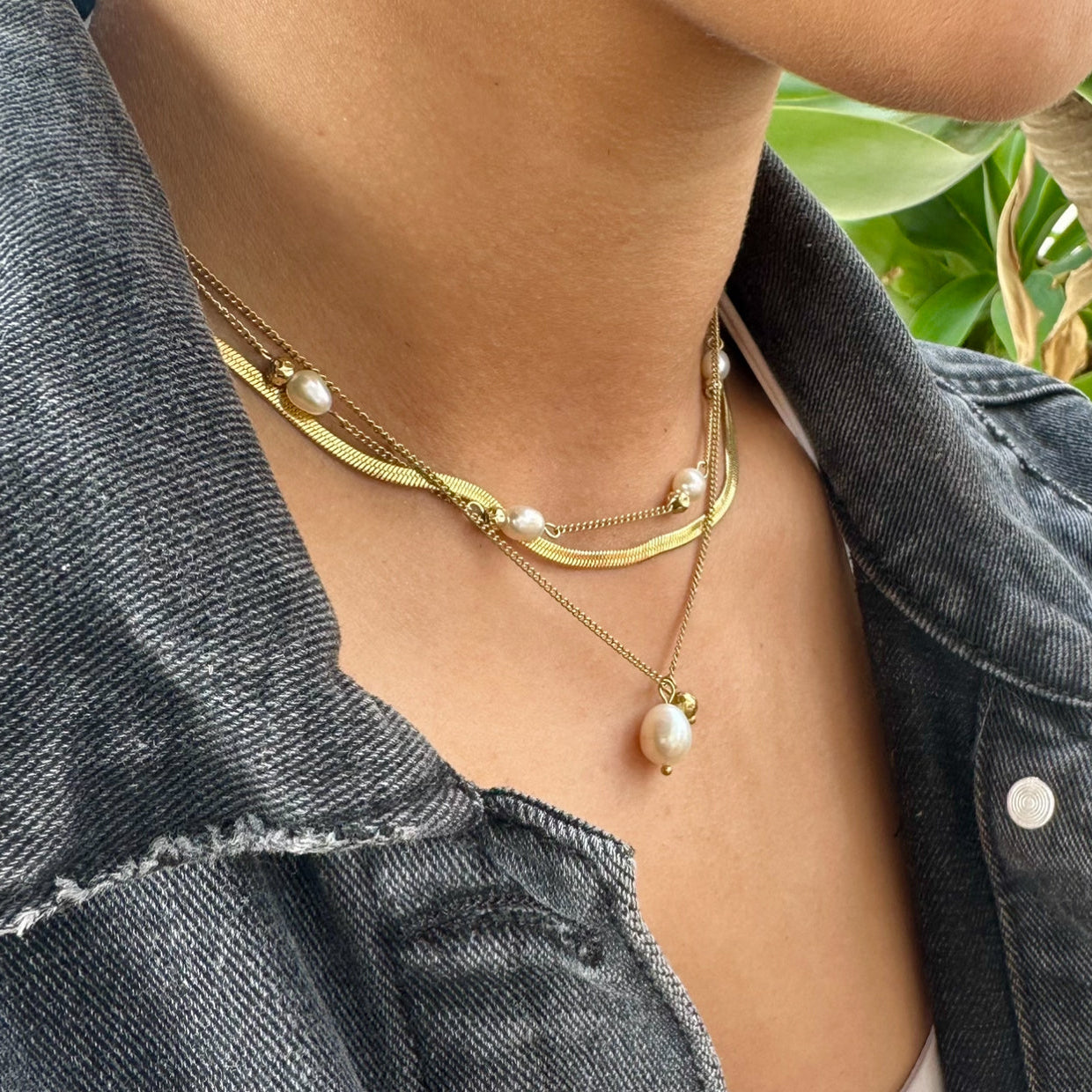 Person wearing Sidewalk gold necklace with pearl beads against a denim jacket background