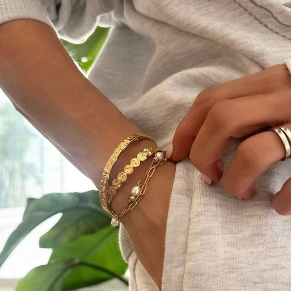 Close-up of a person's wrist wearing gold bracelets with a blurred natural background