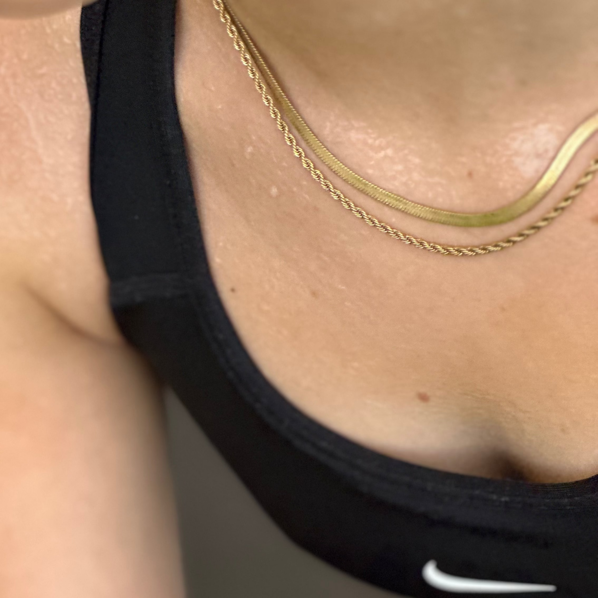 Close-up of a person wearing a gold necklace and black tank top with a Nike logo.