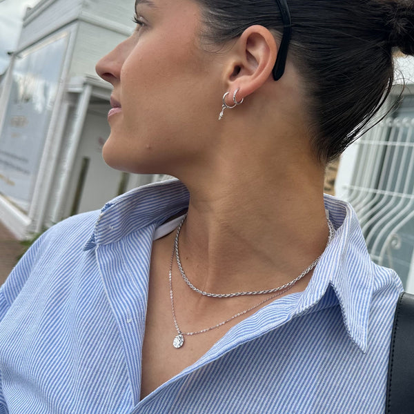 Woman wearing a blue striped shirt and layered Harmony + Perform Silver necklaces with earrings.