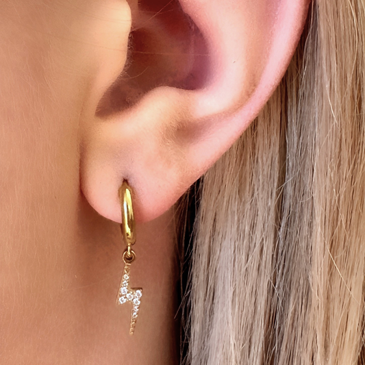 Gold hoop earring with a small pendant worn by a person with blonde hair.