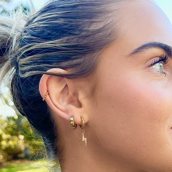 Close-up of a person wearing gold hoop earrings with a blurred natural background