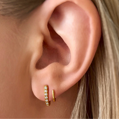 Close-up of an ear wearing gold hoop earrings with a blurred background