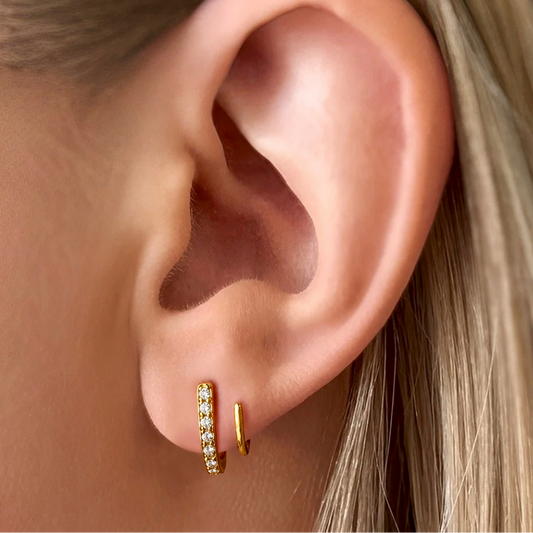 Close-up of an ear wearing gold hoop earrings with a blurred background