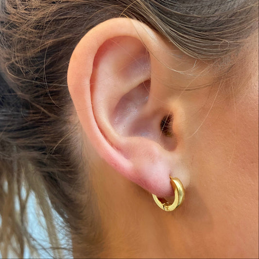 Close-up of an ear wearing gold hoop earrings with a central gemstone.