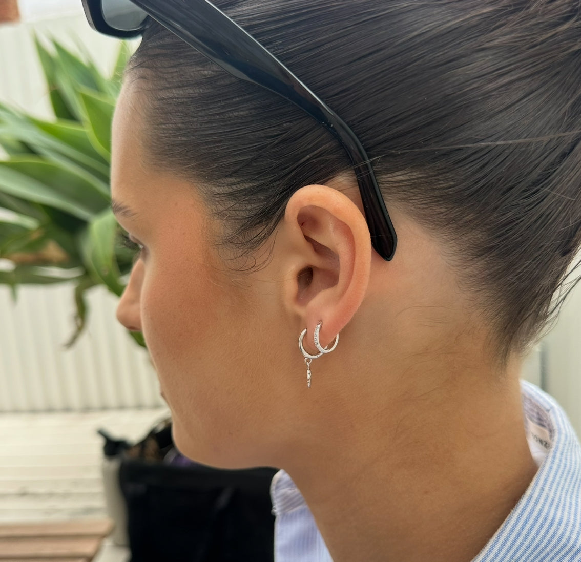 Close-up of a person wearing a silver hoop earring with a plant in the background