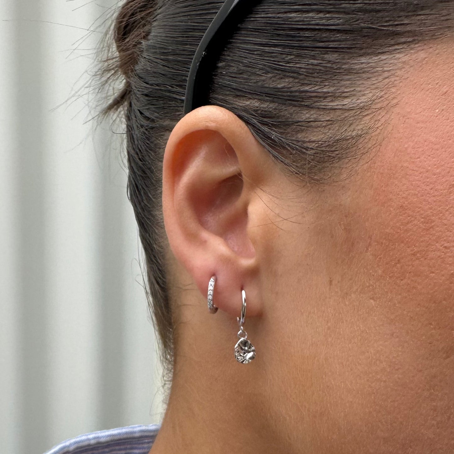 Close-up of a person wearing silver hoop earrings with a blurred background