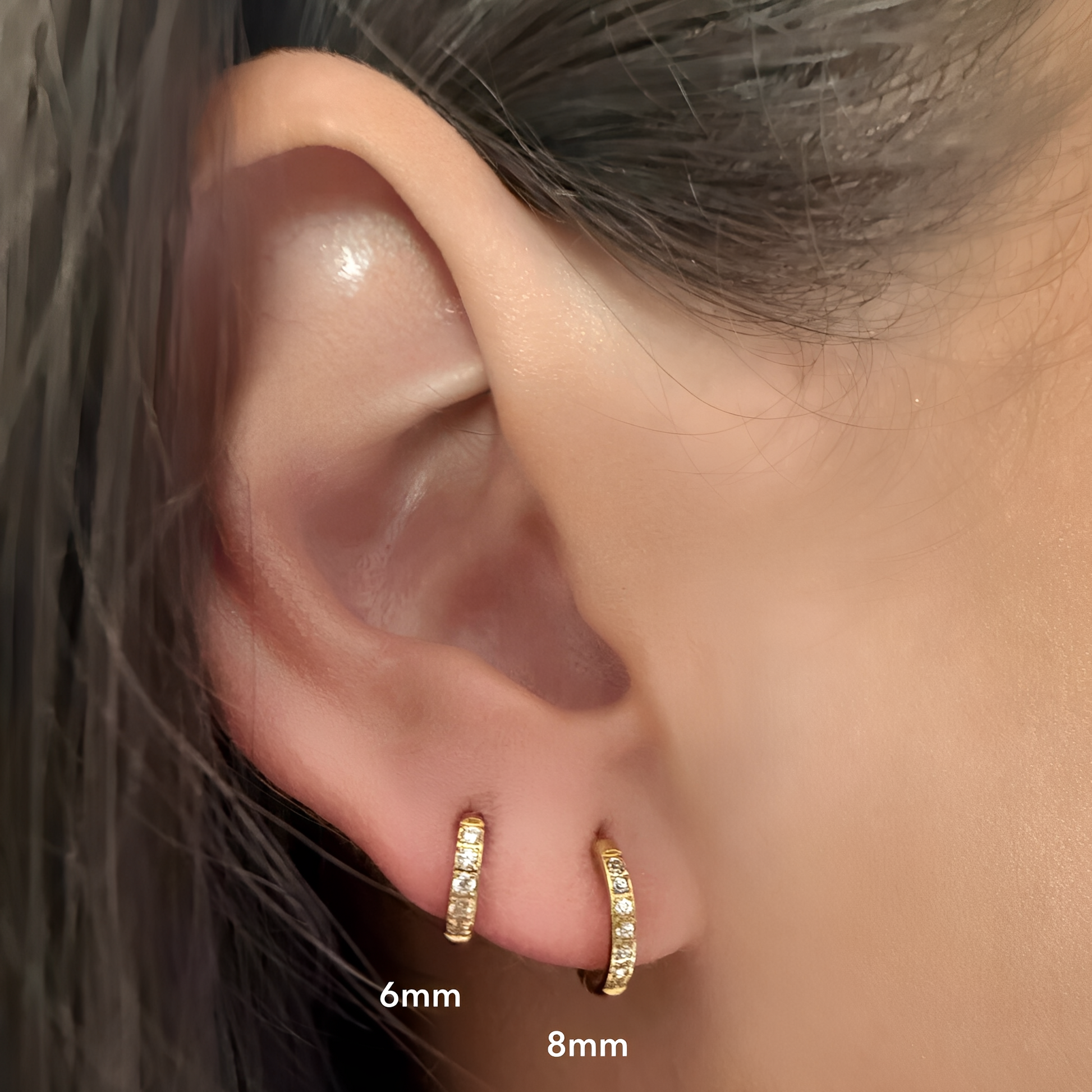 Close-up of an ear wearing gold hoop earrings with size labels.