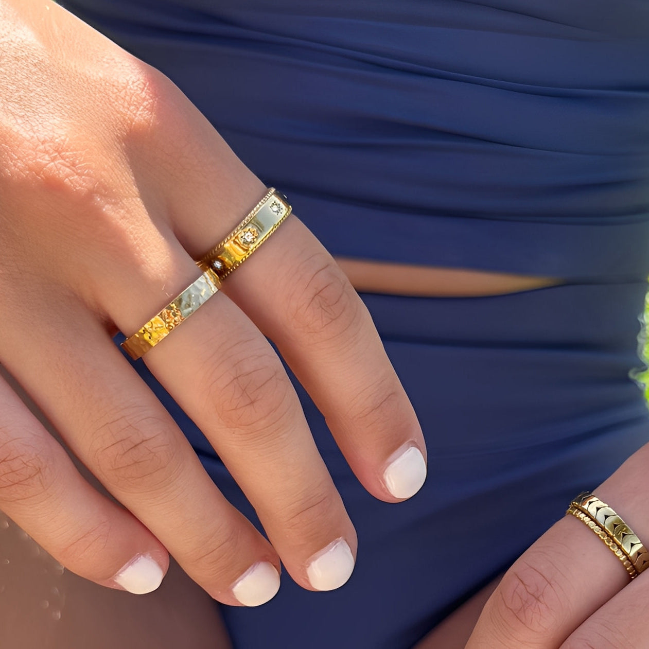 Close-up of a hand wearing two gold rings with a blue background