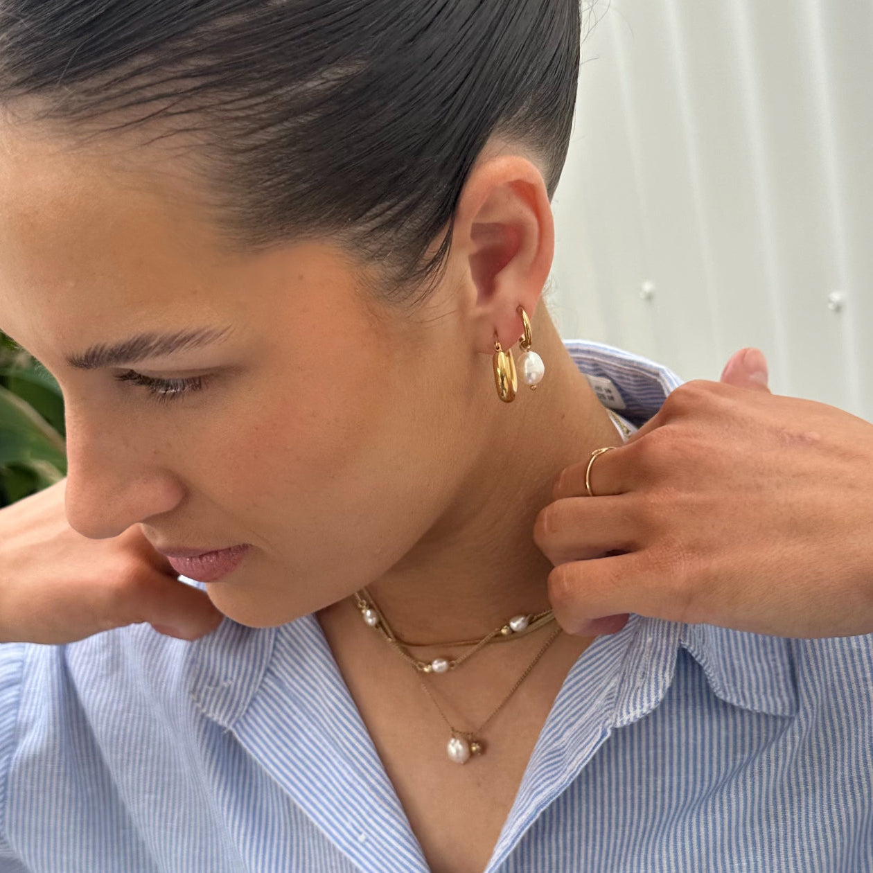 Woman wearing EVER Jewellery After Dark Hoop Earrings in gold with a single pearl drop, styled with layered pearl necklaces.