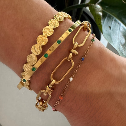 Stacked gold bracelets on a wrist, featuring the EVER Colour Wave Bracelet with multi-coloured beads alongside hammered and emerald-stone gold cuffs.