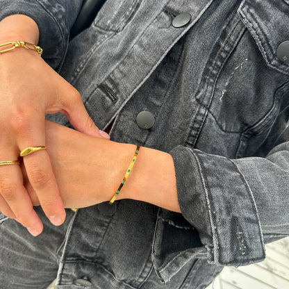 Model wearing EVER Jewellery Playmaker gold cuff bracelet with emerald green stones, styled with a gold ring and black denim jacket.