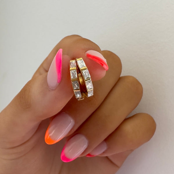 Undefeated Hoop Earrings held between fingers with bright pink manicure, showing gold and stone detail.